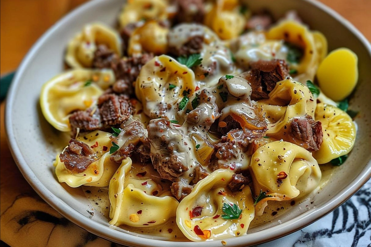 A skillet of cheesy cheesesteak tortellini with steak and vegetables