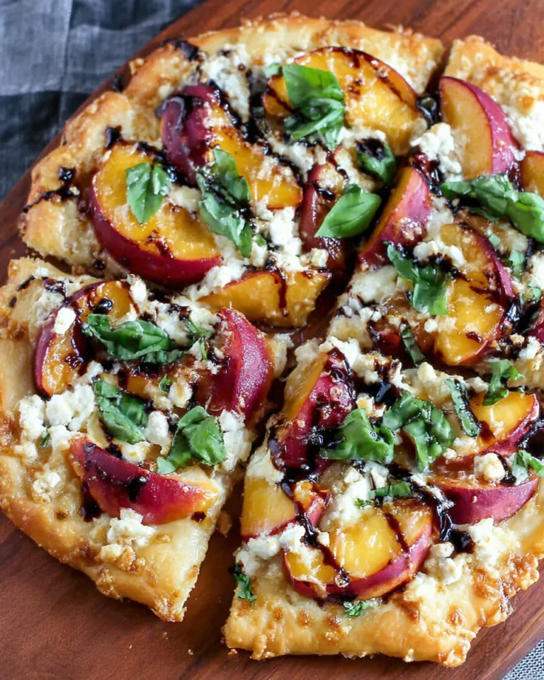 Freshly baked nectarine pizza topped with sliced nectarines, melted cheese, fresh basil, and a glossy drizzle of balsamic reduction on a crisp, golden crust.