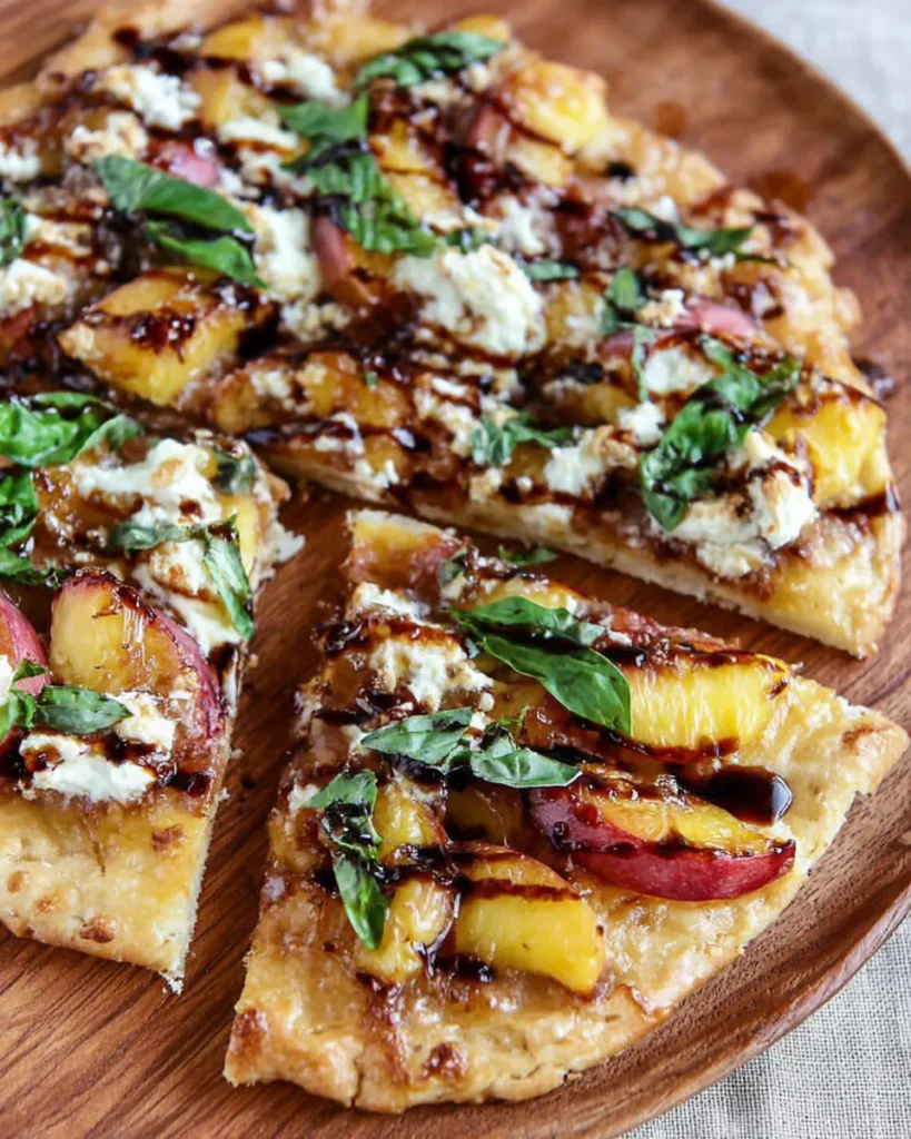 Freshly baked nectarine pizza topped with sliced nectarines, melted cheese, fresh basil, and a glossy drizzle of balsamic reduction on a crisp, golden crust.