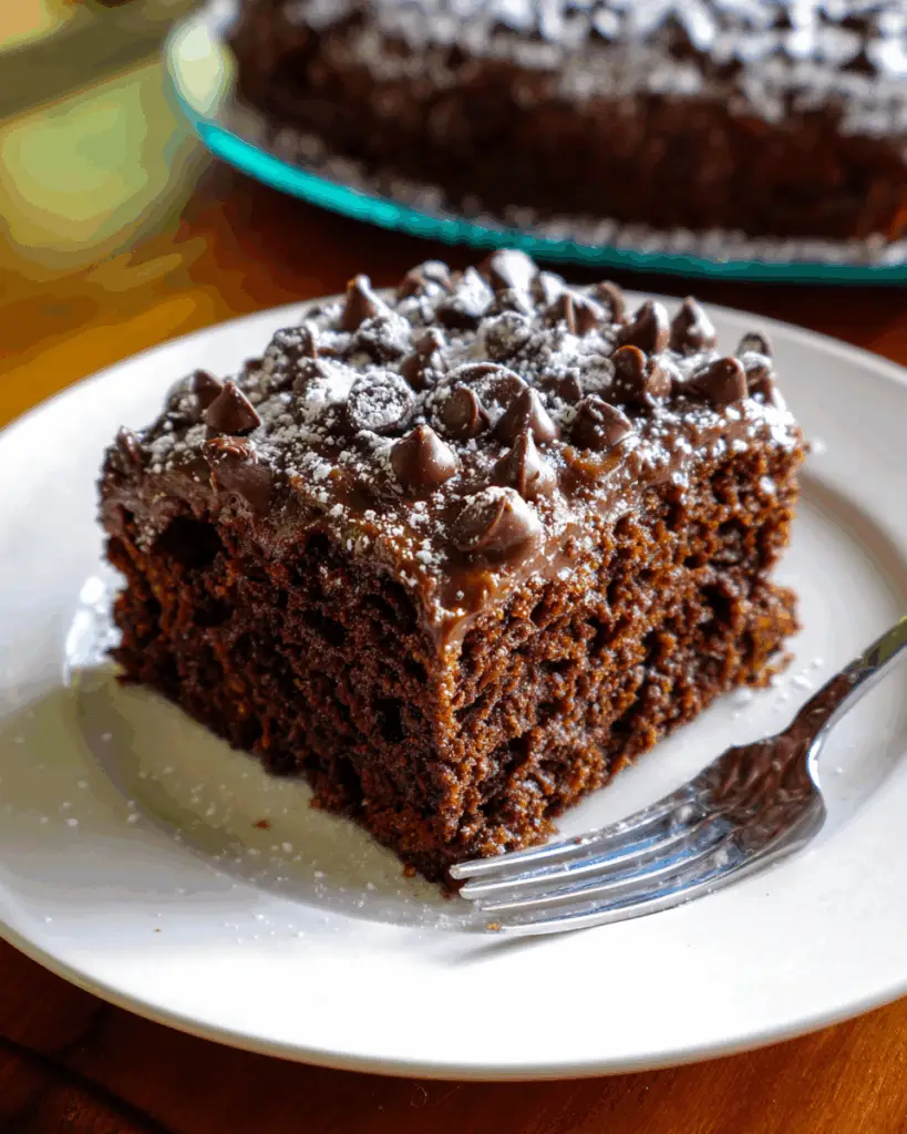 Close-up of a homemade chocolate zucchini cake topped with rich chocolate frosting, showing a moist, dense crumb with tiny flecks of zucchini, captured in soft natural light on a kitchen counter.