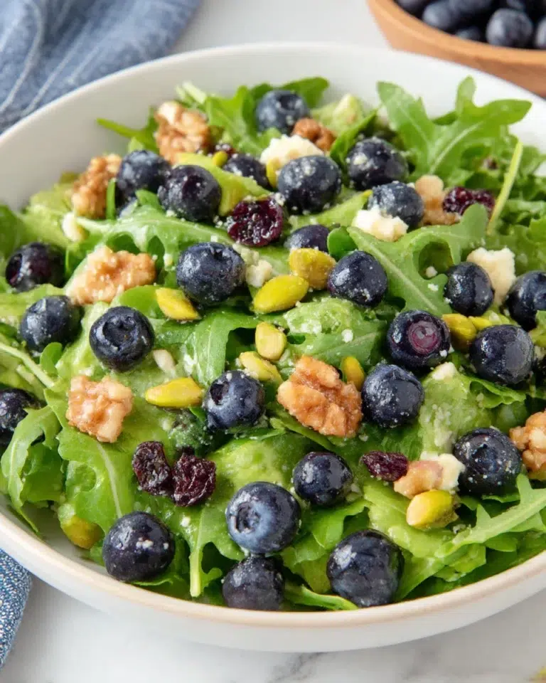 Blueberry pistachio spring salad with fresh greens, feta cheese, and honey balsamic dressing served in a bowl on a white marble counter in natural light
