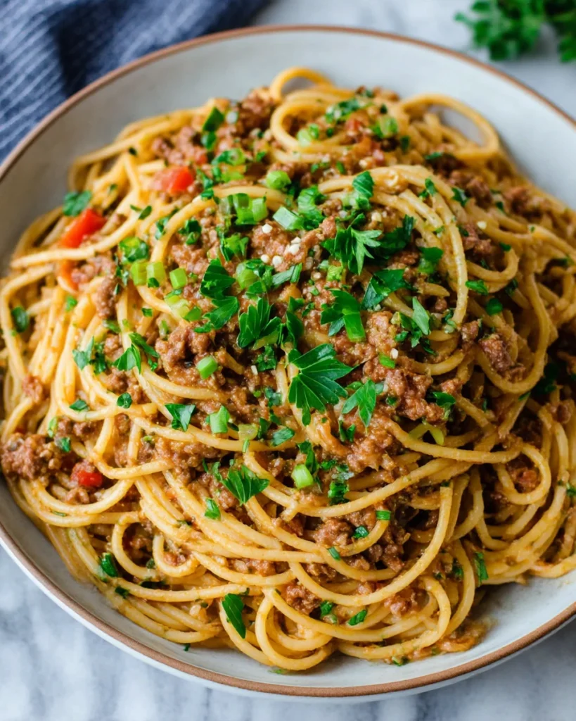 Close-up of homemade dirty spaghetti in a white bowl made with ground beef, spaghetti, and bell peppers, served as a cozy one-pot Cajun pasta meal in a warm kitchen setting.