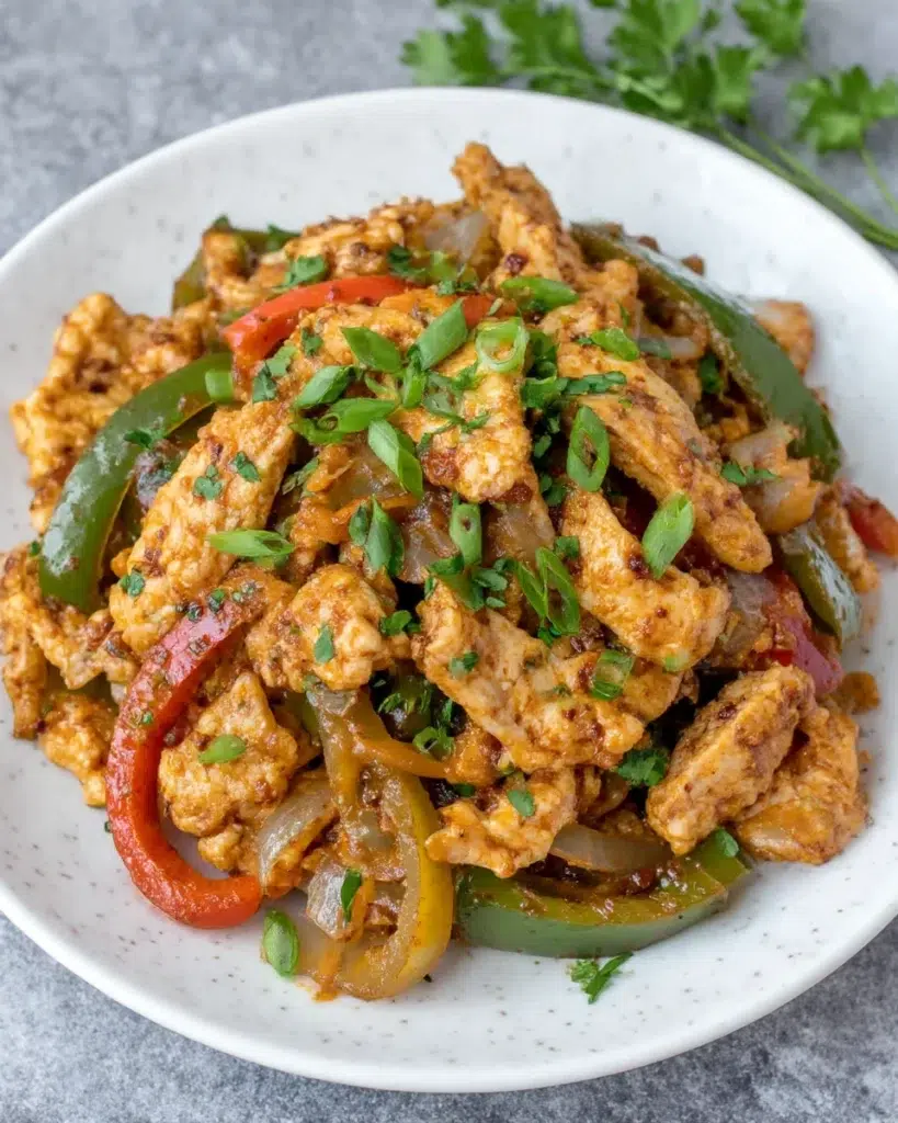 Close-up of a spicy chicken fajita bake with golden melted cheese, tender chicken, and colorful bell peppers in a white baking dish on a marble kitchen counter, natural light, homemade style