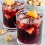 Close-up of a homemade Americano Cocktail served over ice in a highball glass with an orange slice garnish, photographed in natural light on a white marble kitchen counter.