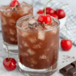 A rich Chocolate Cherry Bourbon Cocktail served over ice in a rocks glass, garnished with a maraschino cherry and shaved chocolate, photographed in natural kitchen light with a cozy homemade feel.
