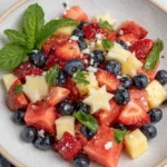Festive 4th of July fruit salad served in a white bowl, featuring juicy watermelon cubes, sliced strawberries, fresh blueberries, star-shaped jicama pieces, and chopped mint. A colorful red, white, and blue patriotic summer dish perfect for Independence Day celebrations, backyard barbecues, picnics, and holiday gatherings.