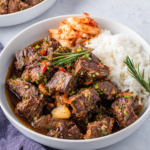Close-up of Korean Style Pot Roast served over white rice with kimchi and fresh cilantro, featuring tender shredded beef coated in a rich glossy gochujang sauce in a cozy home kitchen setting.