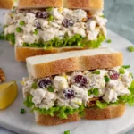 Close-up of homemade Simple Chicken Salad Tea Sandwiches made with diced chicken, dried cranberries, toasted pecans, scallions, and creamy mayonnaise filling on soft white bread, photographed in natural kitchen lighting on a white marble counter.