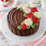 Beautiful homemade Mother’s Day Cake decorated with pink and red buttercream flowers on top of soft vanilla cake with chocolate buttercream frosting, photographed in natural kitchen lighting on a white marble counter.