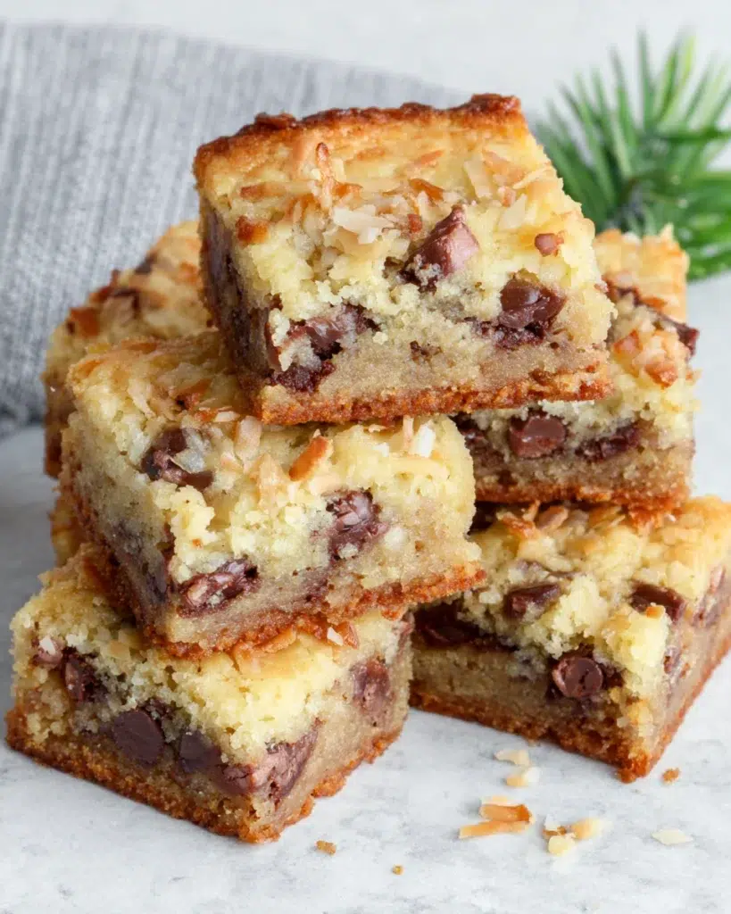 Freshly baked Coconut Toffee Chocolate Chip Cookie Bars on a white marble countertop, featuring golden brown edges, melted chocolate chips, crunchy toffee bits, and toasted coconut flakes. Homemade dessert photographed in natural window light with a warm kitchen atmosphere and soft background blur.