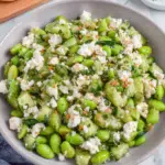 Fresh edamame salad with cucumbers, feta cheese, and herbs in a bowl, light and healthy Mediterranean-style dish with vibrant green colors and a homemade rustic presentation.