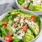 Fresh Green Goddess Avocado Salad served in a bowl with crisp romaine lettuce, creamy avocado, cucumber, cherry tomatoes, mixed seeds, and a homemade avocado herb dressing, photographed in natural light on a white marble countertop.