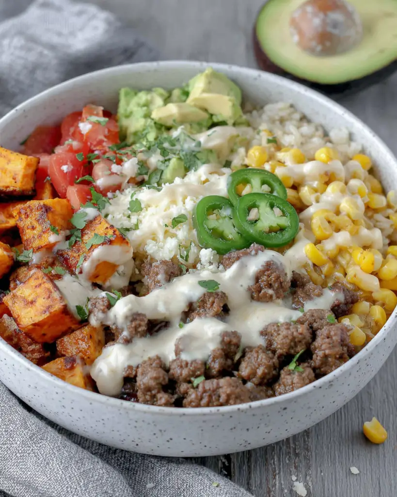 Ground Beef Sweet Potato Taco Bowl with Lime Crema topped with seasoned ground beef, roasted sweet potatoes, black beans, corn, rice, avocado, fresh cilantro, and creamy lime sauce in a homemade Mexican-inspired dinner bowl.