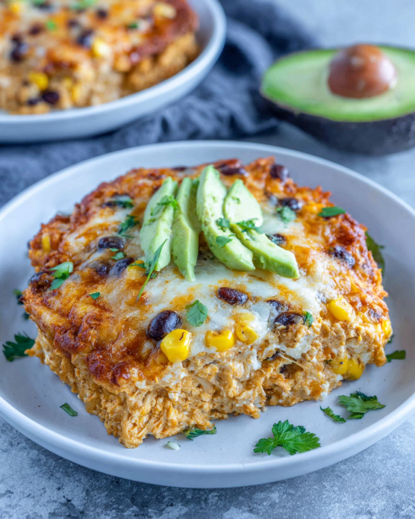 High-Protein Cottage Cheese Enchilada Bake topped with melted cheese, avocado, cilantro, black beans, and corn in a white baking dish on a marble countertop.