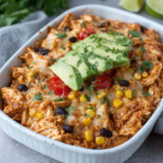 High-Protein Cottage Cheese Enchilada Bake topped with melted cheese, avocado, cilantro, black beans, and corn in a white baking dish on a marble countertop.
