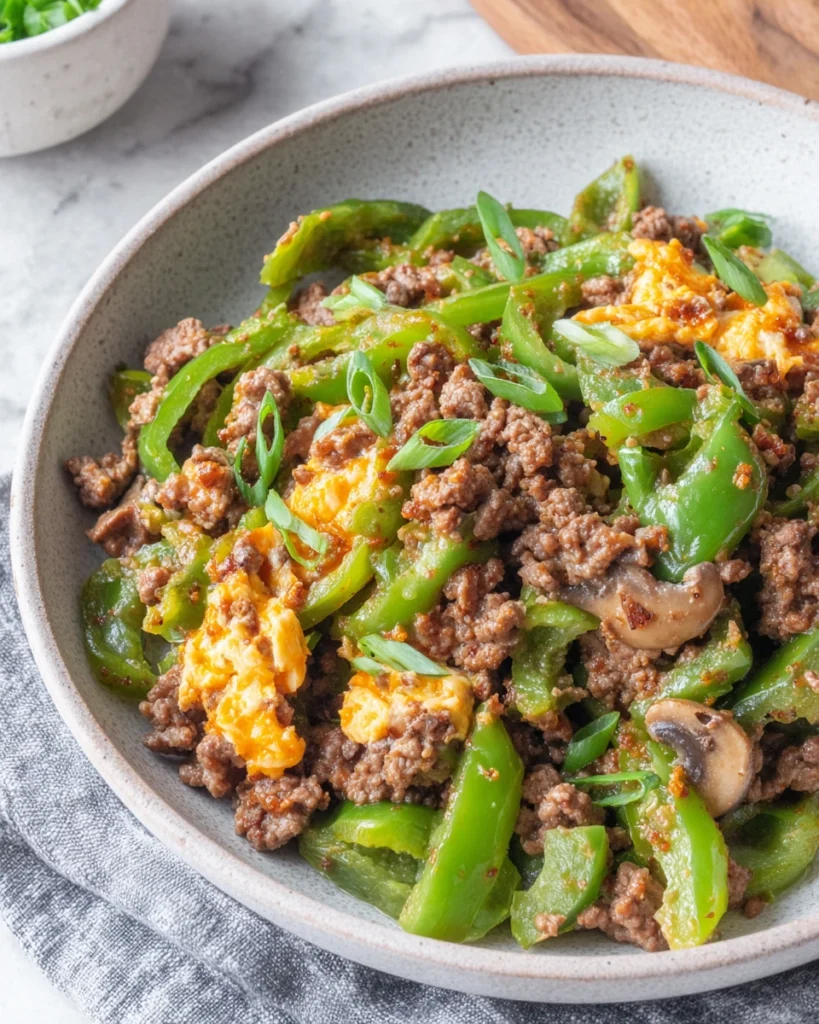 Overhead view of Philly Cheesesteak Bowls in a white bowl filled with ground beef, sautéed green peppers, mushrooms, and melted provolone cheese served in a cozy home kitchen with natural lighting.