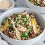 Overhead view of Philly Cheesesteak Bowls in a white bowl filled with ground beef, sautéed green peppers, mushrooms, and melted provolone cheese served in a cozy home kitchen with natural lighting.