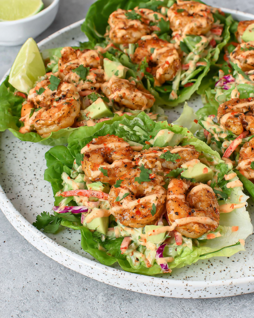 Sheet Pan Chili-Lime Shrimp Lettuce Wraps filled with juicy roasted shrimp, crunchy red cabbage and radish slaw, and creamy avocado sriracha crema served in fresh butter lettuce leaves on a white plate with natural kitchen lighting.