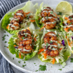 Sheet Pan Chili-Lime Shrimp Lettuce Wraps filled with juicy roasted shrimp, crunchy red cabbage and radish slaw, and creamy avocado sriracha crema served in fresh butter lettuce leaves on a white plate with natural kitchen lighting.