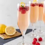 French Kiss Cocktail served in a champagne flute with fresh muddled raspberries, sparkling Champagne, and a lemon twist garnish. A refreshing and elegant raspberry cocktail perfect for celebrations, brunches, parties, and special occasions.