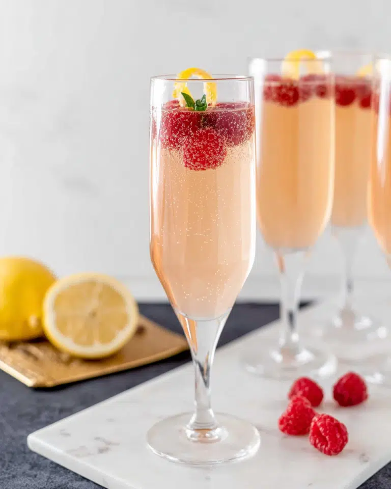 French Kiss Cocktail served in a champagne flute with fresh muddled raspberries, sparkling Champagne, and a lemon twist garnish. A refreshing and elegant raspberry cocktail perfect for celebrations, brunches, parties, and special occasions.