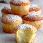 Fluffy Japanese Cotton Cheesecake Cupcakes with golden tops and an airy soufflé-like texture, arranged in paper liners on a white marble countertop. The cupcakes feature a light, creamy interior and a delicate cream cheese flavor, photographed in natural window light for a warm homemade baking scene.