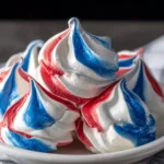 Close-up of red, white, and blue meringue kisses on a white marble kitchen counter, showing crisp airy textures and delicate swirls with soft natural window light in a cozy homemade setting.