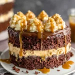 A thick slice of Chocolate Whiskey Cake with Salted Caramel Buttercream and dark chocolate ganache on a white plate. The moist chocolate cake layers are filled with creamy salted caramel frosting and topped with glossy chocolate ganache drips, creating an elegant homemade dessert perfect for celebrations and special occasions.