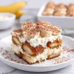 Close-up of homemade Bourbon Banana Pudding Tiramisu layered with coffee-soaked ladyfingers, creamy mascarpone filling, fresh banana slices, and a generous dusting of cocoa powder in a baking dish.