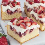 Keto Strawberry Shortcake Bars topped with fresh chopped strawberries and a fluffy cream cheese whipped topping on a buttery almond flour crust, served on a white plate in natural light.
