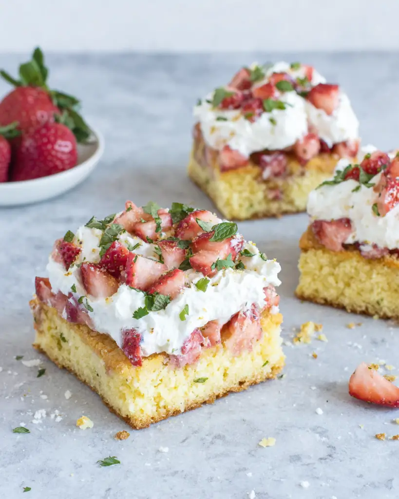 Keto Strawberry Shortcake Bars topped with fresh chopped strawberries and a fluffy cream cheese whipped topping on a buttery almond flour crust, served on a white plate in natural light.