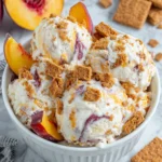 Creamy No-Churn Peach Cheesecake Ice Cream served in a white bowl with fresh peach swirls, chopped Biscoff cookies, and juicy peach slices on top. This easy homemade frozen dessert has a rich cheesecake flavor and requires no ice cream maker.