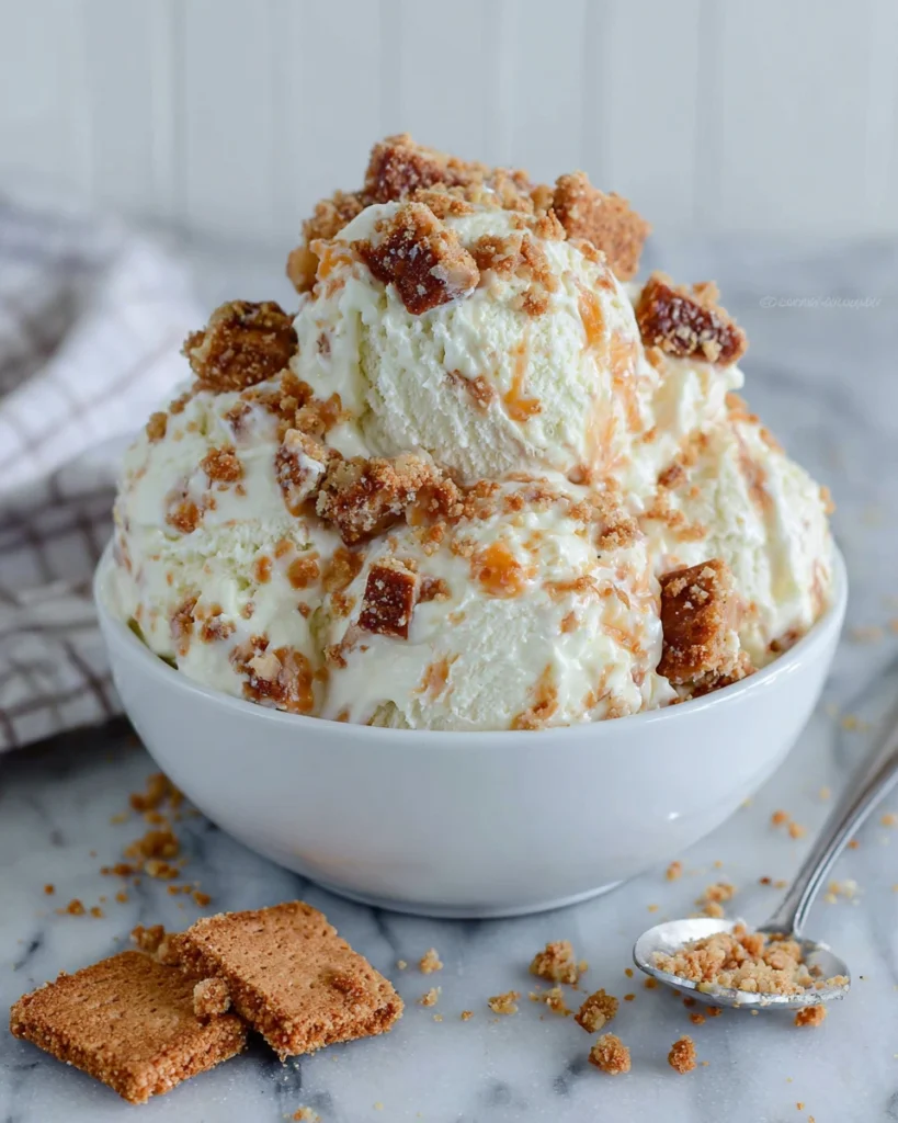 Creamy No-Churn Peach Cheesecake Ice Cream served in a white bowl with fresh peach swirls, chopped Biscoff cookies, and juicy peach slices on top. This easy homemade frozen dessert has a rich cheesecake flavor and requires no ice cream maker.