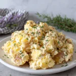A bowl of creamy Simple Vegan Potato Salad made with Yukon Gold potatoes, tahini, cashew butter, fresh dill, basil, oregano, and chives, served in a rustic bowl on a white marble countertop in natural light.