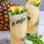 A refreshing Vodka Pineapple Basil Smash Cocktail served in a Collins glass with fresh pineapple, basil leaves, Meyer lemon slices, and ice. This tropical vodka cocktail is garnished with a pineapple leaf and fresh basil, making it the perfect summer drink for parties, brunch, or happy hour.