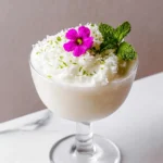 A creamy frozen Bamboo Colada made with amontillado sherry, sweetened coconut cream, sweet vermouth, and fresh lime juice, served in a chilled cocktail glass and garnished with an edible flower on a white marble countertop in natural light.
