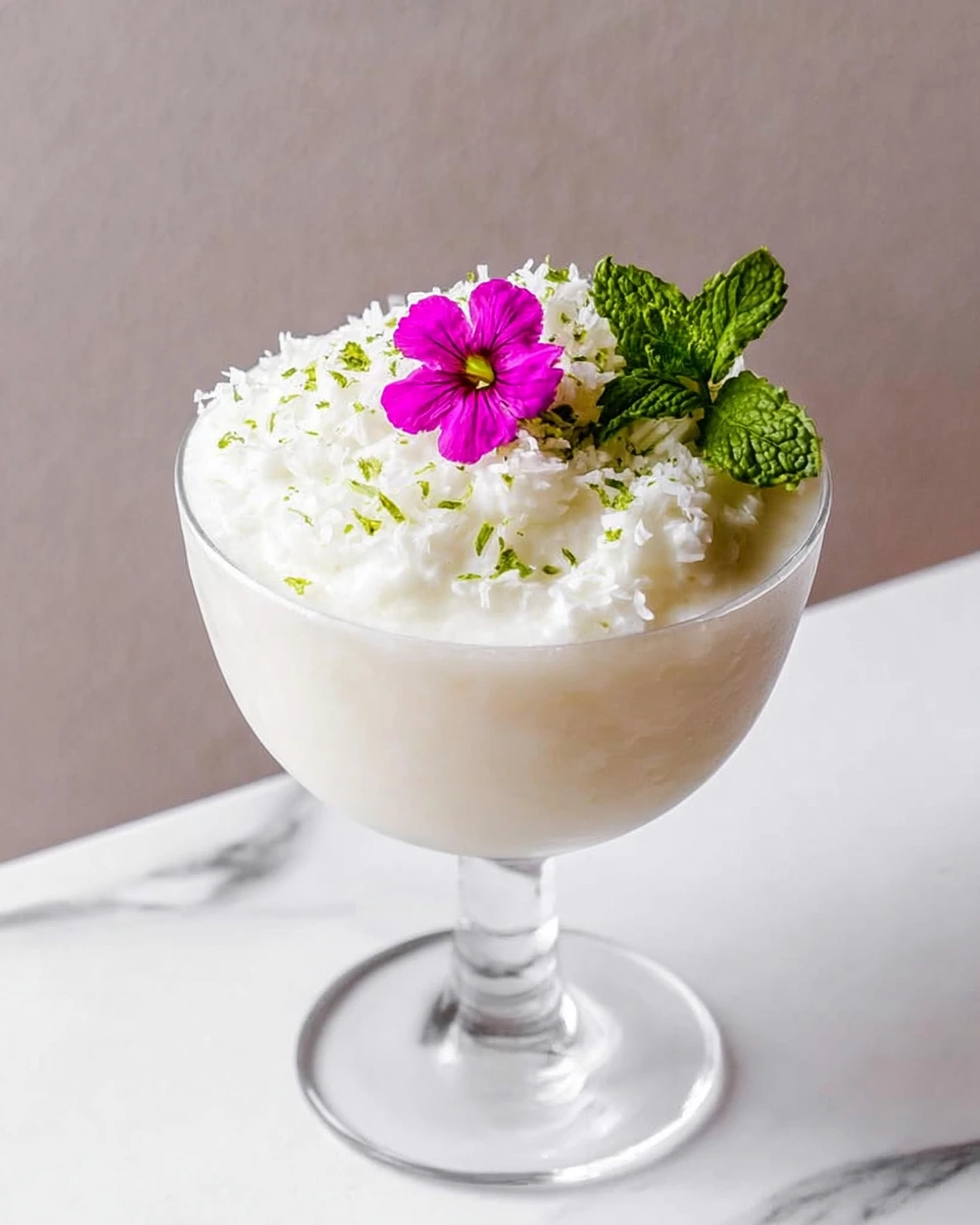 A creamy frozen Bamboo Colada made with amontillado sherry, sweetened coconut cream, sweet vermouth, and fresh lime juice, served in a chilled cocktail glass and garnished with an edible flower on a white marble countertop in natural light.