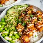 Honey Sriracha Salmon Bowls served with caramelized salmon bites over fluffy white rice, fresh avocado, cucumber, edamame, and a drizzle of sriracha mayo in a homemade-style bowl.