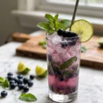 Blueberry Keto Mojito served over crushed ice in a clear highball glass, made with fresh blueberries, mint leaves, lime juice, white rum, and club soda. A refreshing sugar-free summer cocktail garnished with fresh blueberries and mint on a white marble countertop.