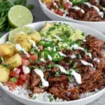 Crockpot Chipotle Pineapple Pot Roast Bowls with shredded beef, caramelized pineapple, avocado salsa, jalapeño, cilantro, rice, and creamy bang bang sauce served in a bowl.