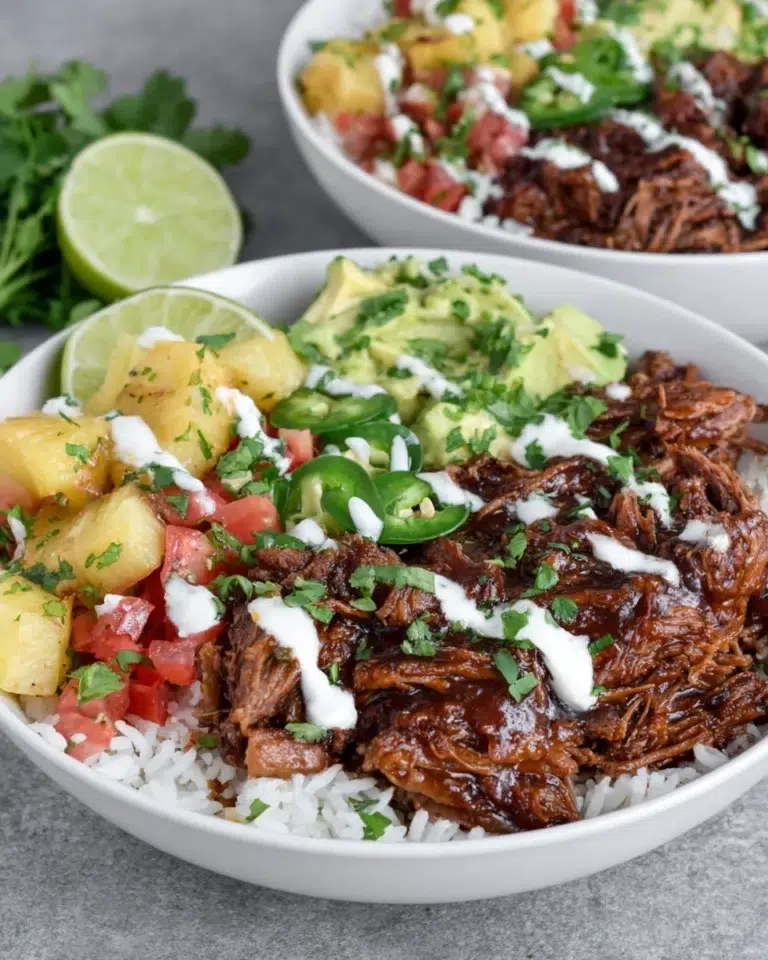 Crockpot Chipotle Pineapple Pot Roast Bowls with shredded beef, caramelized pineapple, avocado salsa, jalapeño, cilantro, rice, and creamy bang bang sauce served in a bowl.