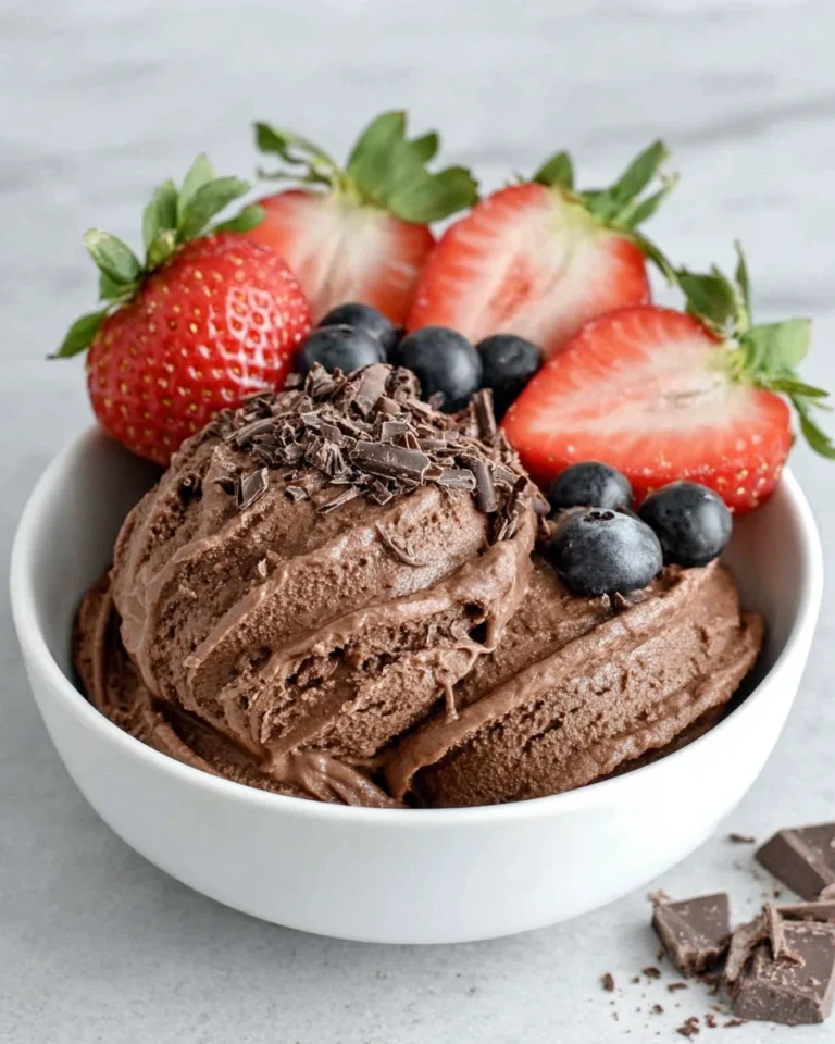 A bowl of creamy homemade chocolate frozen yogurt topped with dark chocolate shavings and fresh strawberries on a white marble countertop in a bright home kitchen.