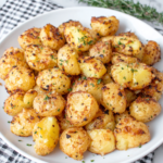 Garlic butter potatoes with golden crispy edges and tender centers, roasted with garlic, butter, thyme, rosemary, and fresh parsley on a white plate.