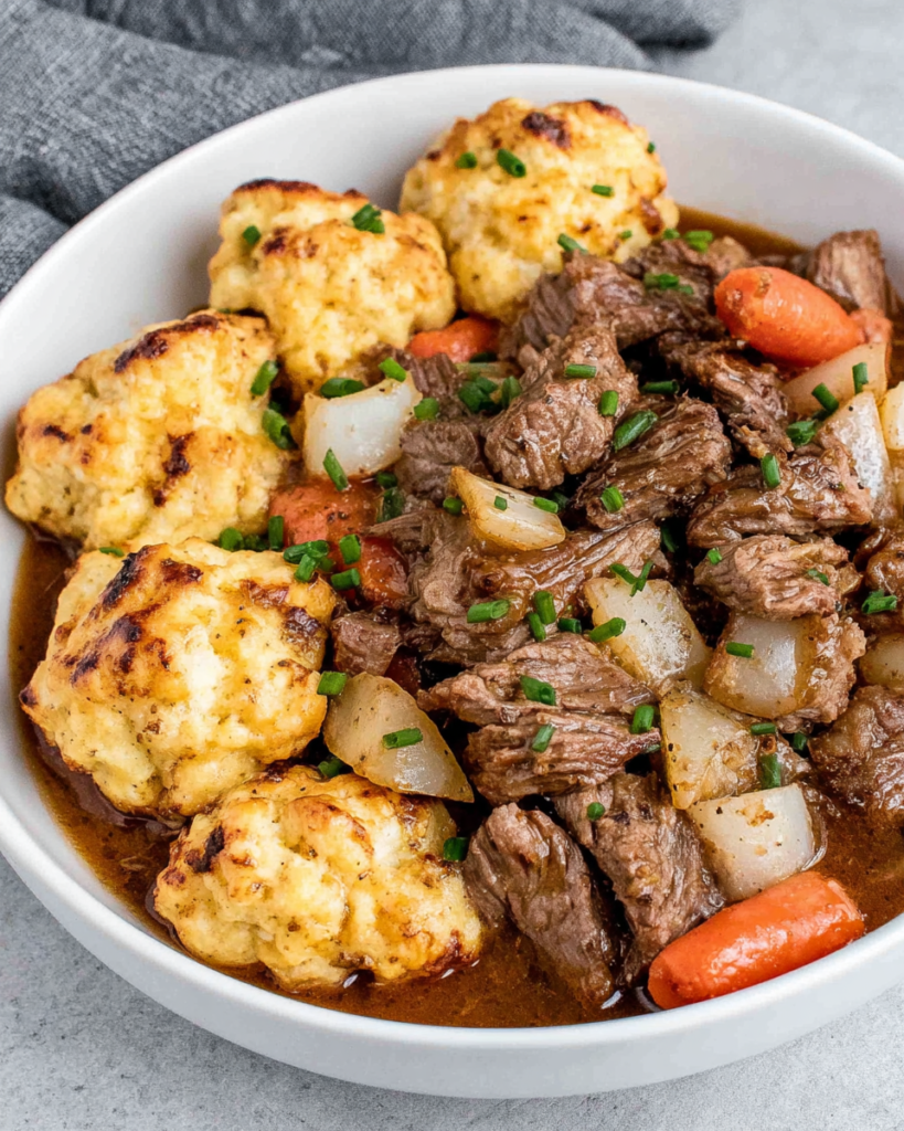 Irish beef stew with tender chunks of beef, carrots, potatoes, celery, and mushrooms in a rich Guinness broth, topped with fluffy cheddar chive dumplings and served in a Dutch oven.