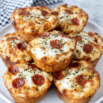 Soft homemade lunchbox pizza muffins with melted mozzarella, mini pepperoni, pizza sauce, and golden-brown tops, arranged on a white marble kitchen counter.