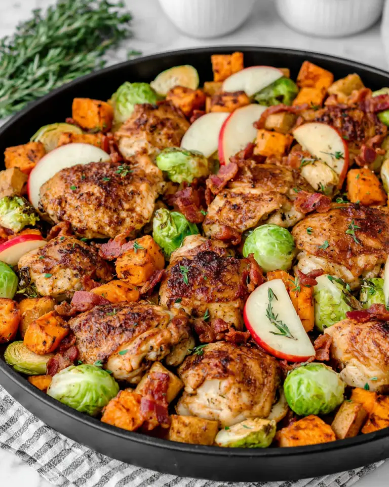 One Pan Autumn Chicken Dinner with golden roasted chicken thighs, sweet potatoes, Brussels sprouts, sliced Fuji apples, shallots, and crispy bacon arranged on a baking sheet.