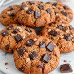 A plate of homemade pumpkin chocolate chip cookies with lightly browned edges and visible milk chocolate chips, arranged on a white marble kitchen counter in natural window light.