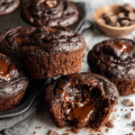 Double Chocolate Muffins with gooey chocolate fudge centers arranged on a white marble kitchen counter, with one muffin cut open to show the rich chocolate filling.