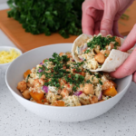 Chickpea smash with roasted pumpkin served in a wrap on a white marble kitchen counter, showing creamy chickpeas, pumpkin cubes, gherkins, parsley, and fresh herbs in natural window light.