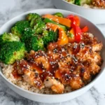 Healthy Sticky Chicken Bowls served with tender glazed chicken, brown rice, broccoli, bell peppers, and sesame seeds in a white bowl for a quick and healthy dinner recipe.